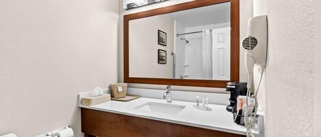 Un baño con tocador de madera, un espejo grande, un secador de pelo y un perchero para toallas.