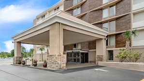 A modern hotel entrance with a covered driveway, stone pillars, and potted plants.