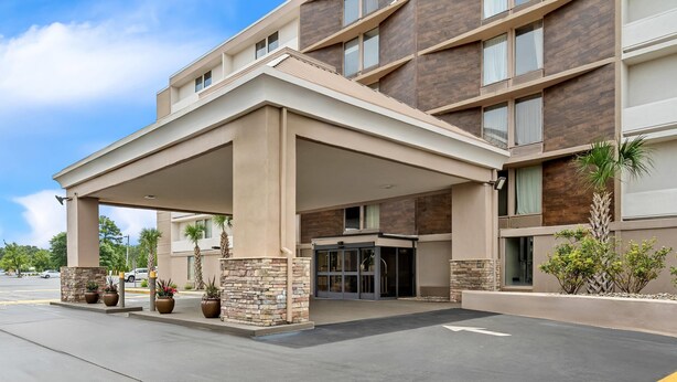 A modern hotel entrance with a covered driveway, stone pillars, and potted plants.