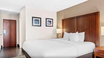 Una camera d'albergo con un letto grande, una testiera in legno, due lampade ai comodini e una porta che dà su un'altra stanza.