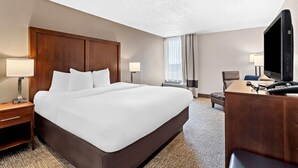 Une chambre d’hôtel avec un grand lit, deux tables de chevet avec des lampes, un bureau avec un ordinateur et un téléphone, et une télévision.