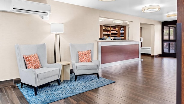 A hotel lobby with two armchairs, a reception desk, and a mirror reflecting the interior.
