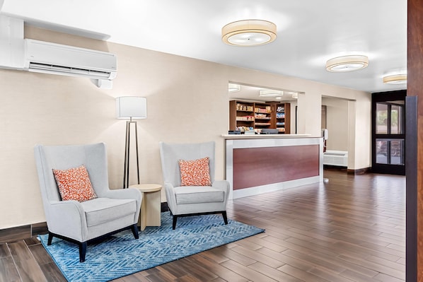 A hotel lobby with two armchairs, a reception desk, and a mirror reflecting the interior.