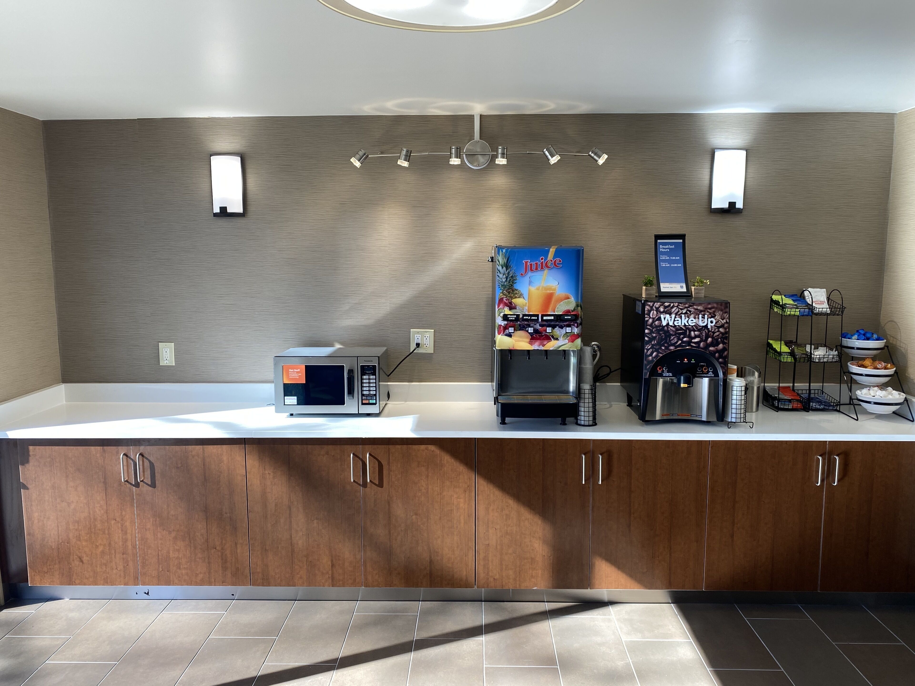 A modern kitchen with a microwave, juice dispenser, and coffee maker on a counter.