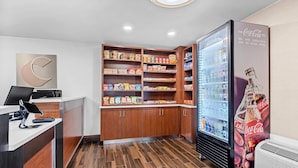 A modern reception area with a wooden counter, a Coca-Cola refrigerator, and a snack shelf.