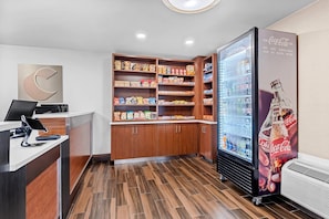 A modern reception area with a wooden counter, a Coca-Cola refrigerator, and a snack shelf.