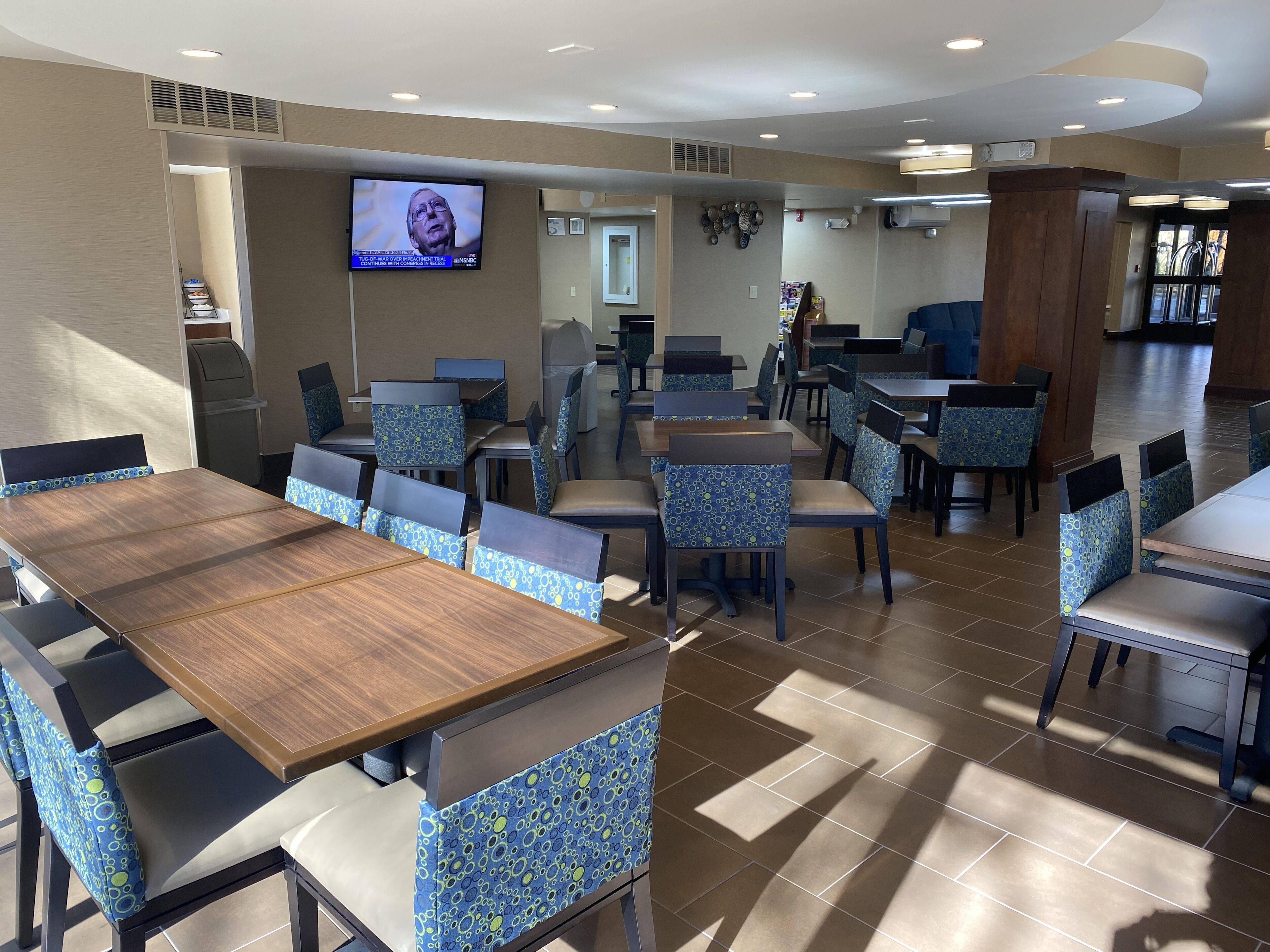 A restaurant with multiple tables and chairs, a television mounted on the wall, and a tiled floor.