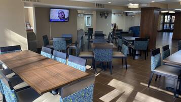 A restaurant with multiple tables and chairs, a television mounted on the wall, and a tiled floor.