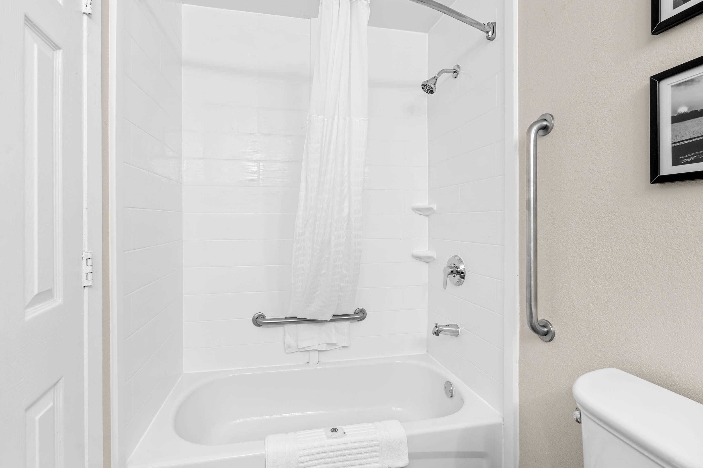 Un baño blanco con una bañera, cortina de ducha, barra de apoyo y un inodoro.