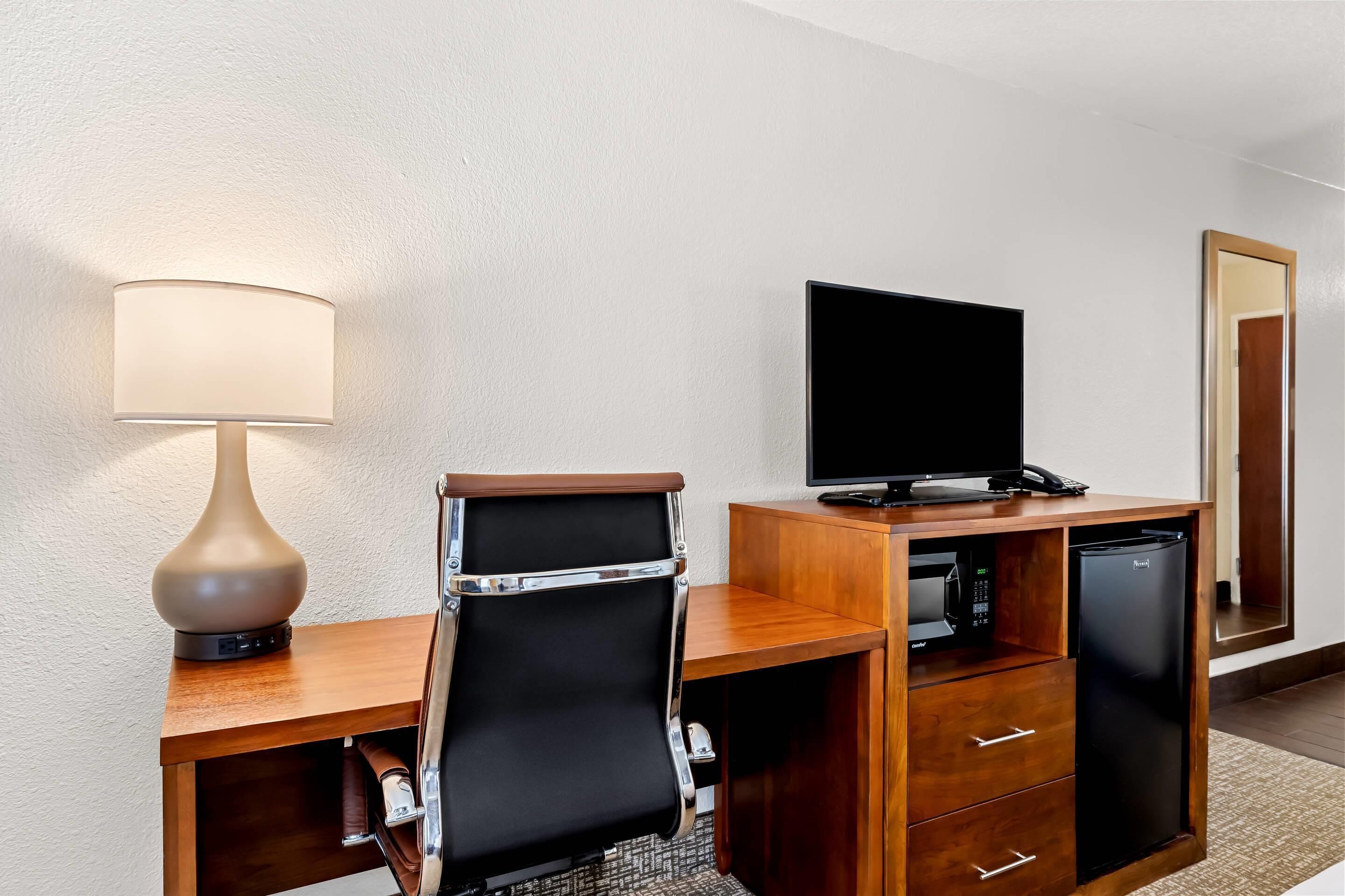 Ein Hotelzimmer mit einem Holzbüro, einem schwarzen Ledersessel, einem Flachbildfernseher, einem kleinen Kühlschrank und einer Lampe.