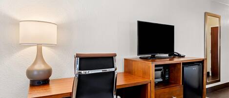 Ein Hotelzimmer mit einem Holzbüro, einem schwarzen Ledersessel, einem Flachbildfernseher, einem kleinen Kühlschrank und einer Lampe.