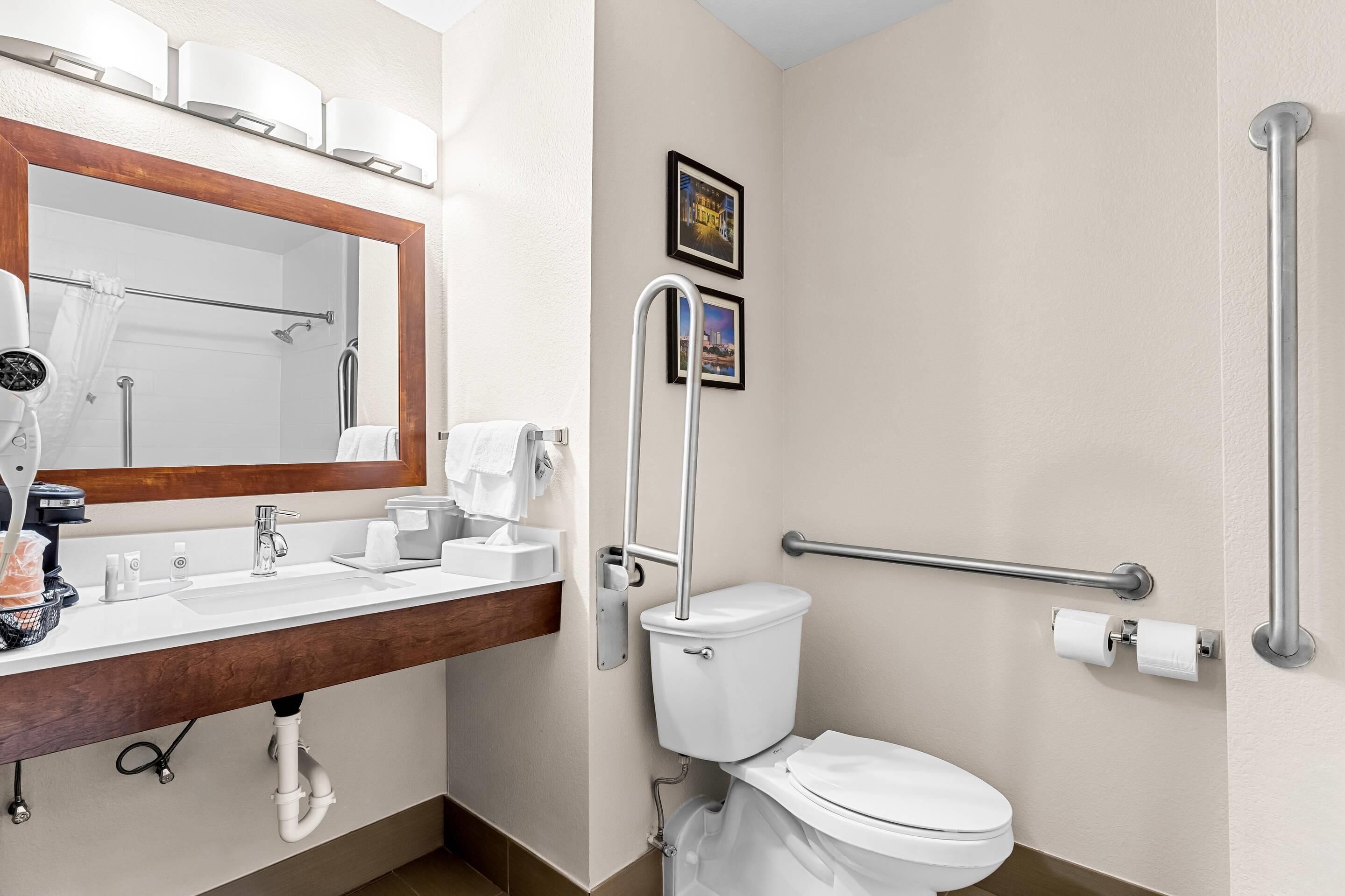 A modern bathroom with a sink, mirror, toilet, and handrails.