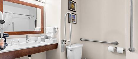 A modern bathroom with a sink, mirror, toilet, and handrails.