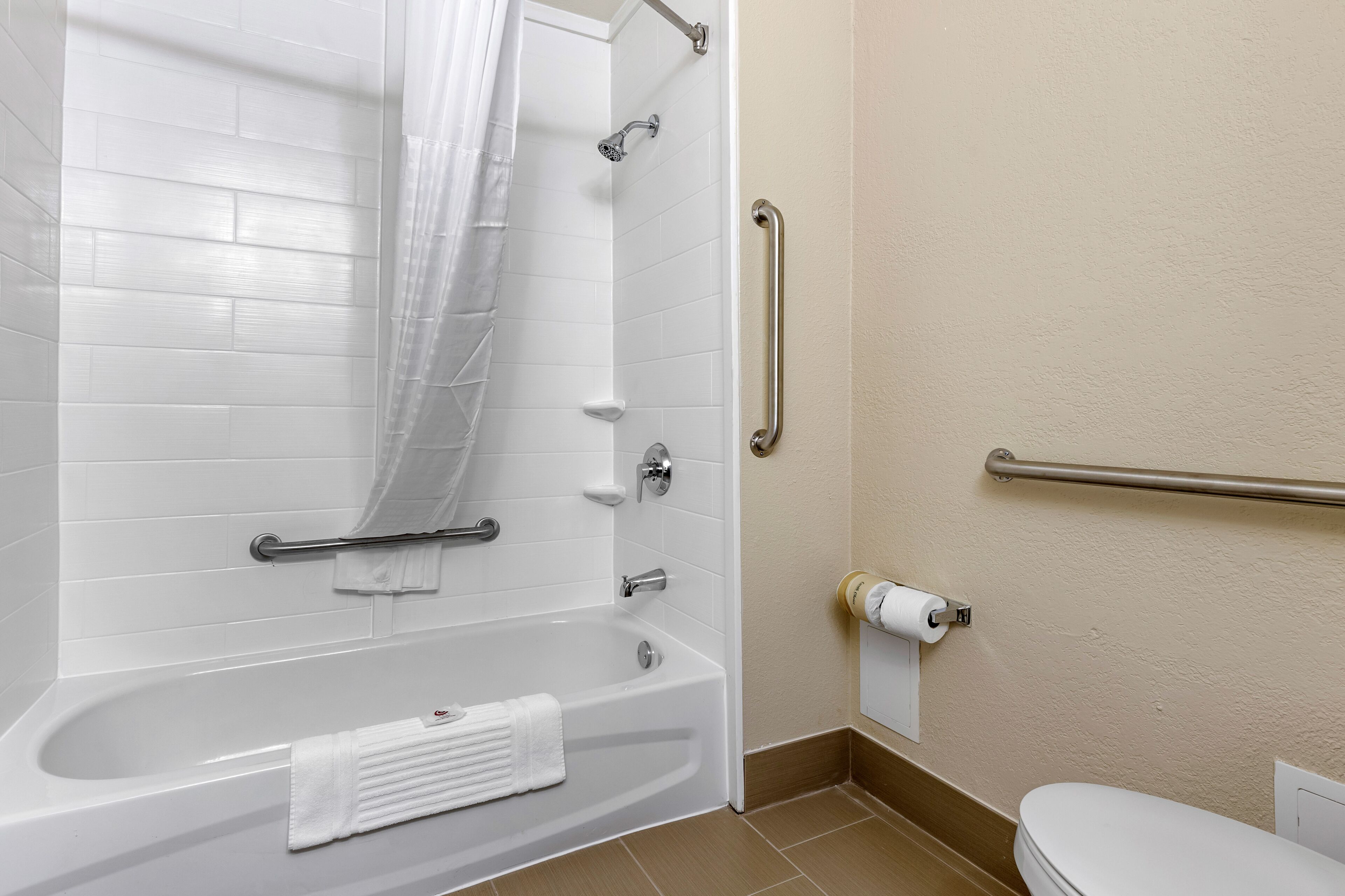 A bathroom with a white bathtub, a shower, a toilet, and a handrail.
