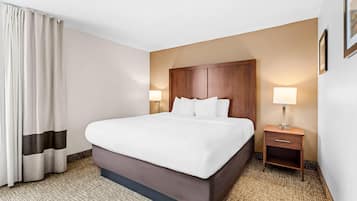 A hotel room with a large bed, a nightstand, a lamp, and a window with curtains.