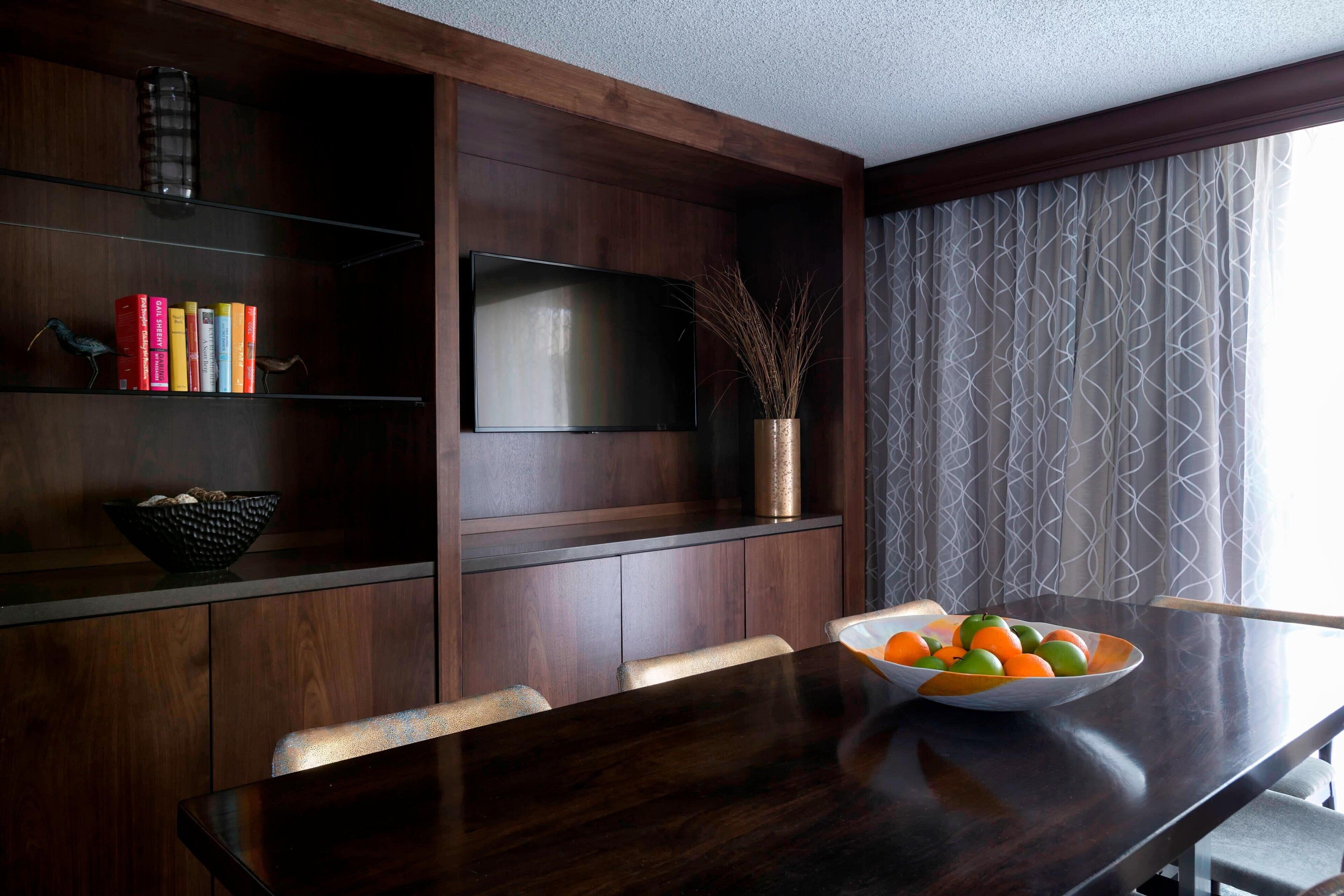 Un área de comedor moderna con una mesa de madera oscura, un cuenco de fruta y un televisor de pantalla plana montado en la pared.