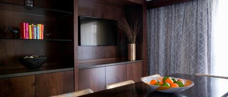 Un área de comedor moderna con una mesa de madera oscura, un cuenco de fruta y un televisor de pantalla plana montado en la pared.