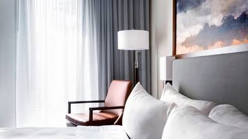 Habitación de hotel con cama, una silla, una lámpara y un cuadro en la pared.
