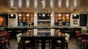 A bar area with a long counter, multiple seating options, and a variety of bottles and glasses.