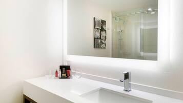 Un baño moderno con un lavabo blanco, un espejo grande y una cabina de ducha de vidrio.