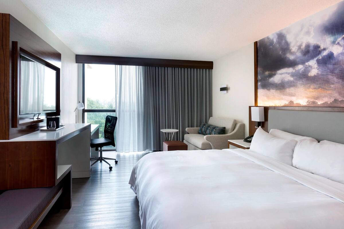 A hotel room with a large bed, a desk, a chair, a small table, and a painting on the wall.
