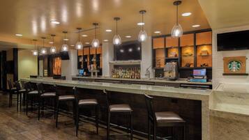 A bar area with a long counter, multiple hanging pendant lights, and bar stools.