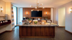 A modern kitchen with a central island, wooden paneling, a chandelier, and a flat-screen TV.