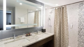 Un baño con un espejo grande, dos lavamanos, una ducha y cortinas con estampado.