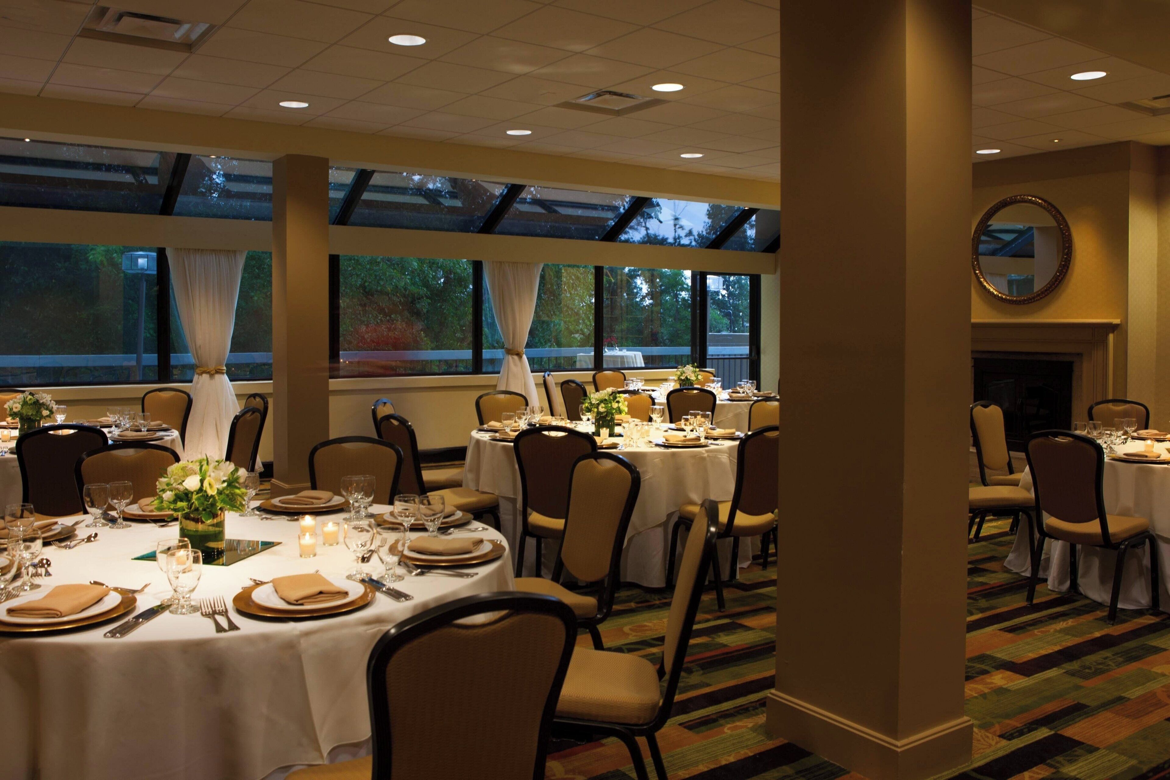 A dining area with round tables set for a meal, chairs, and a fireplace.