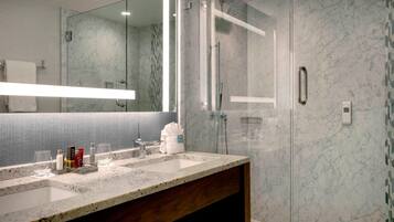 A modern bathroom with a marble countertop, a glass shower enclosure, and a large mirror.