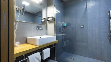 Un baño moderno con un lavabo blanco, una cabina de ducha de vidrio y un espejo con teléfono.