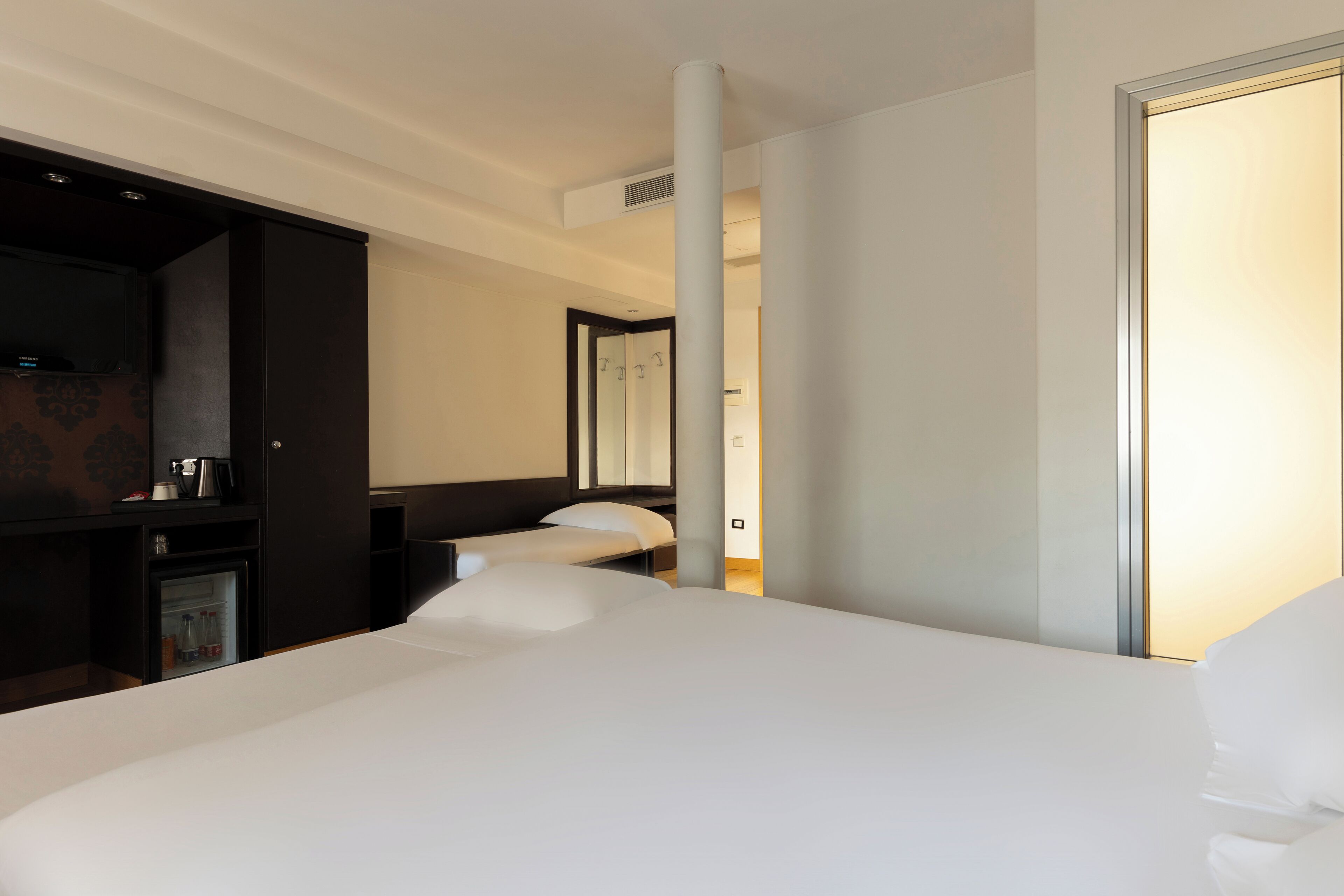 Une chambre d’hôtel avec un grand lit, un petit coin salon, un minibar et un grand miroir.