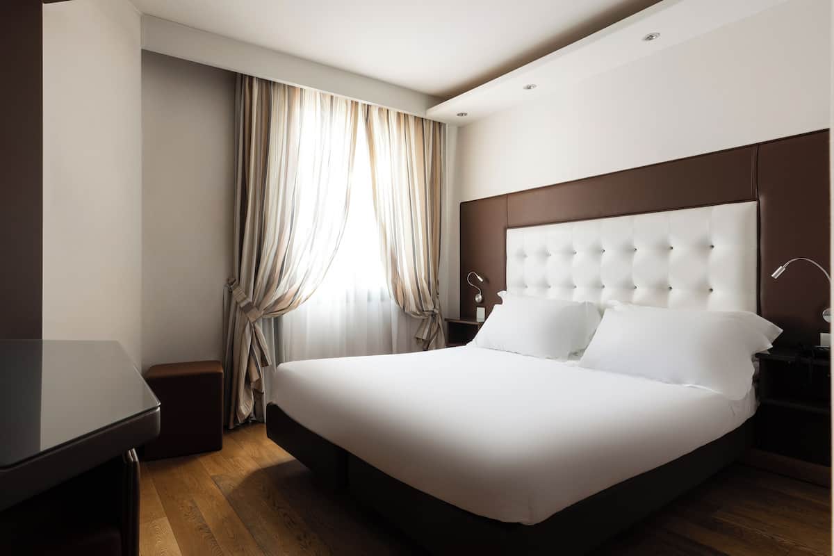 Une chambre d’hôtel moderne avec un grand lit, un bureau et une fenêtre avec des rideaux.
