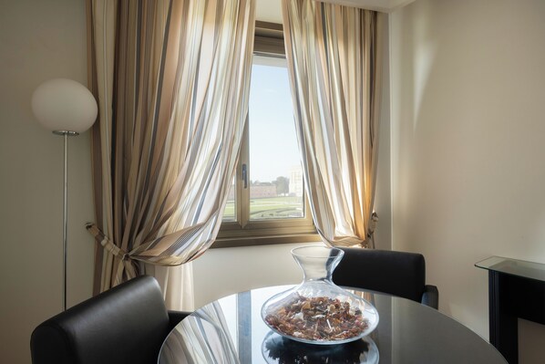 A room with a round table, a glass vase with dried flowers, and a view through a window with curtains.