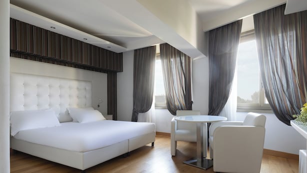 Una habitación de hotel moderna con una cama grande, una mesita redonda pequeña y dos sillas.