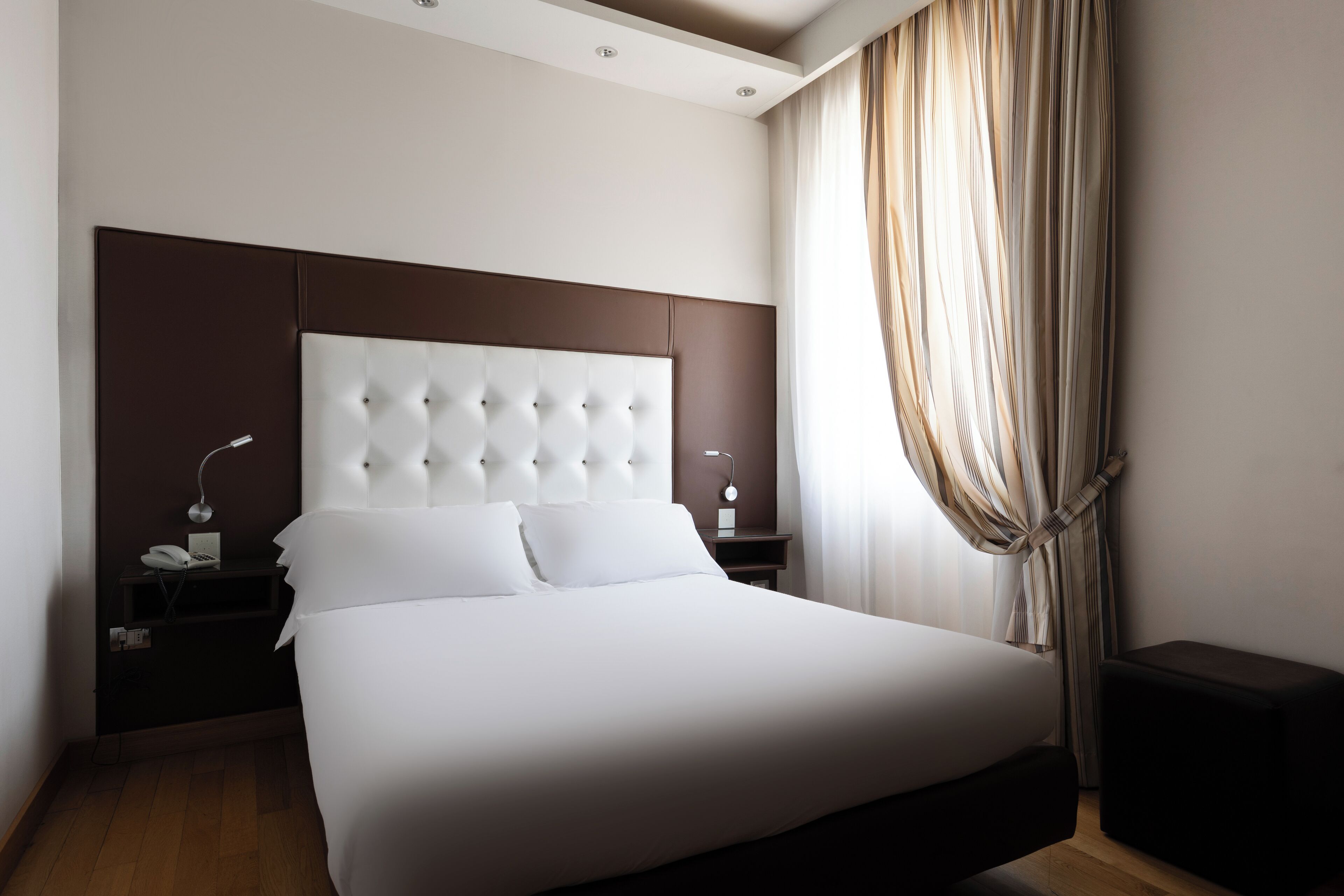 A modern hotel room with a large bed, a nightstand with a lamp, and a small table.