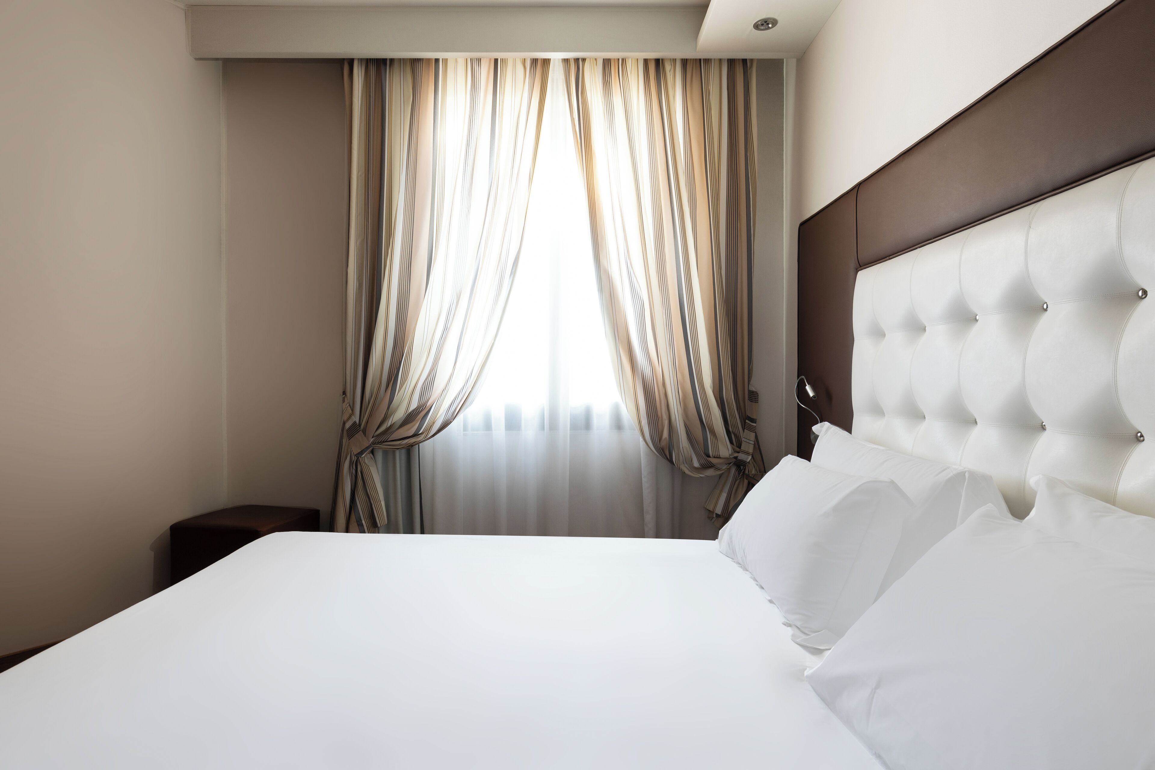 Habitación de hotel con una cama grande, cabecera y cortinas.
