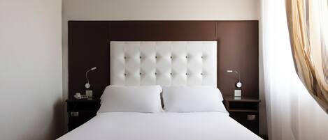 A neatly made bed with a tufted headboard, two bedside tables with lamps, and a curtain on the right.