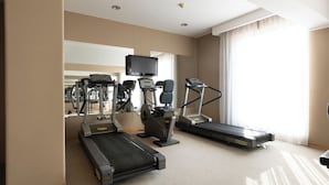 Gimnasio de hotel con cintas de correr, una bicicleta estática y un televisor.