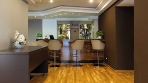 Zona de bar con mostrador de madera, tres taburetes y una recepción.