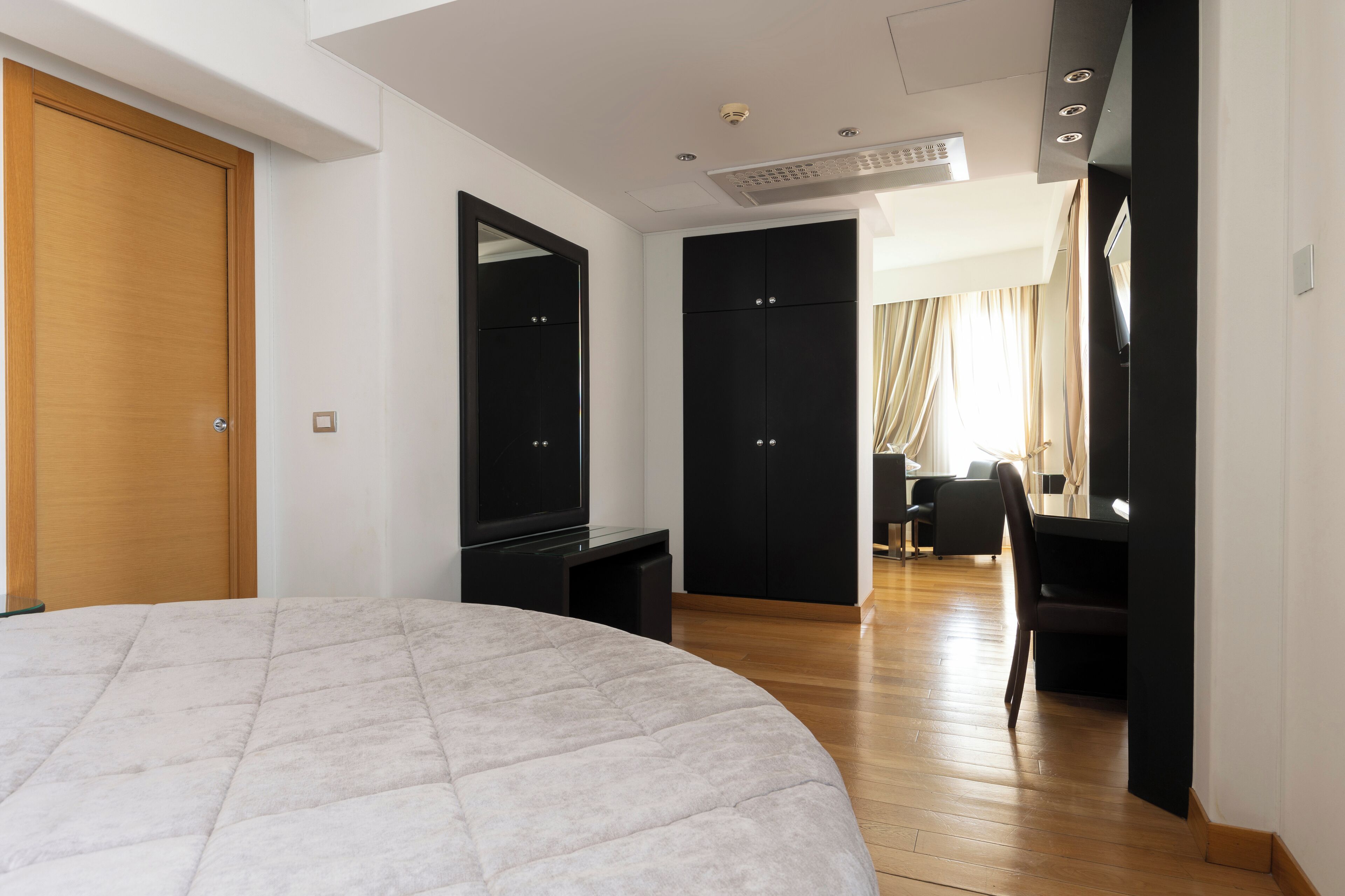 A modern bedroom with a large bed, a TV, a wardrobe, and a desk with a chair.