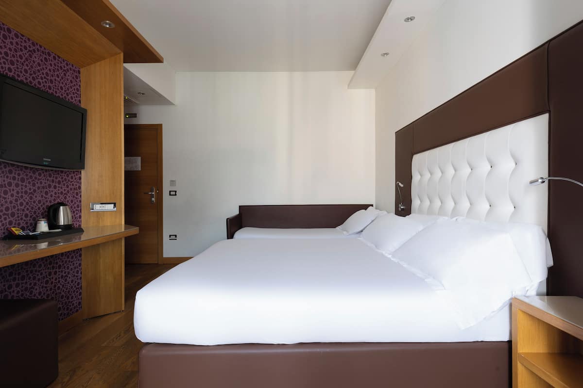 Une chambre d’hôtel moderne dotée d’un grand lit, d’un téléviseur à écran plat, d’un bureau en bois et d’une étagère intégrée.