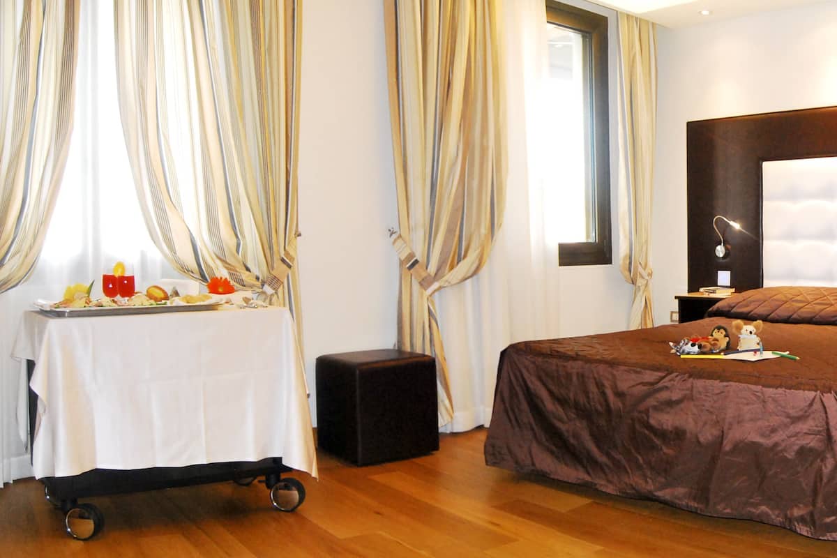 Une chambre avec un grand lit, une table de chevet, une commode, une lampe, une fenêtre avec des rideaux et une table avec de la nourriture.