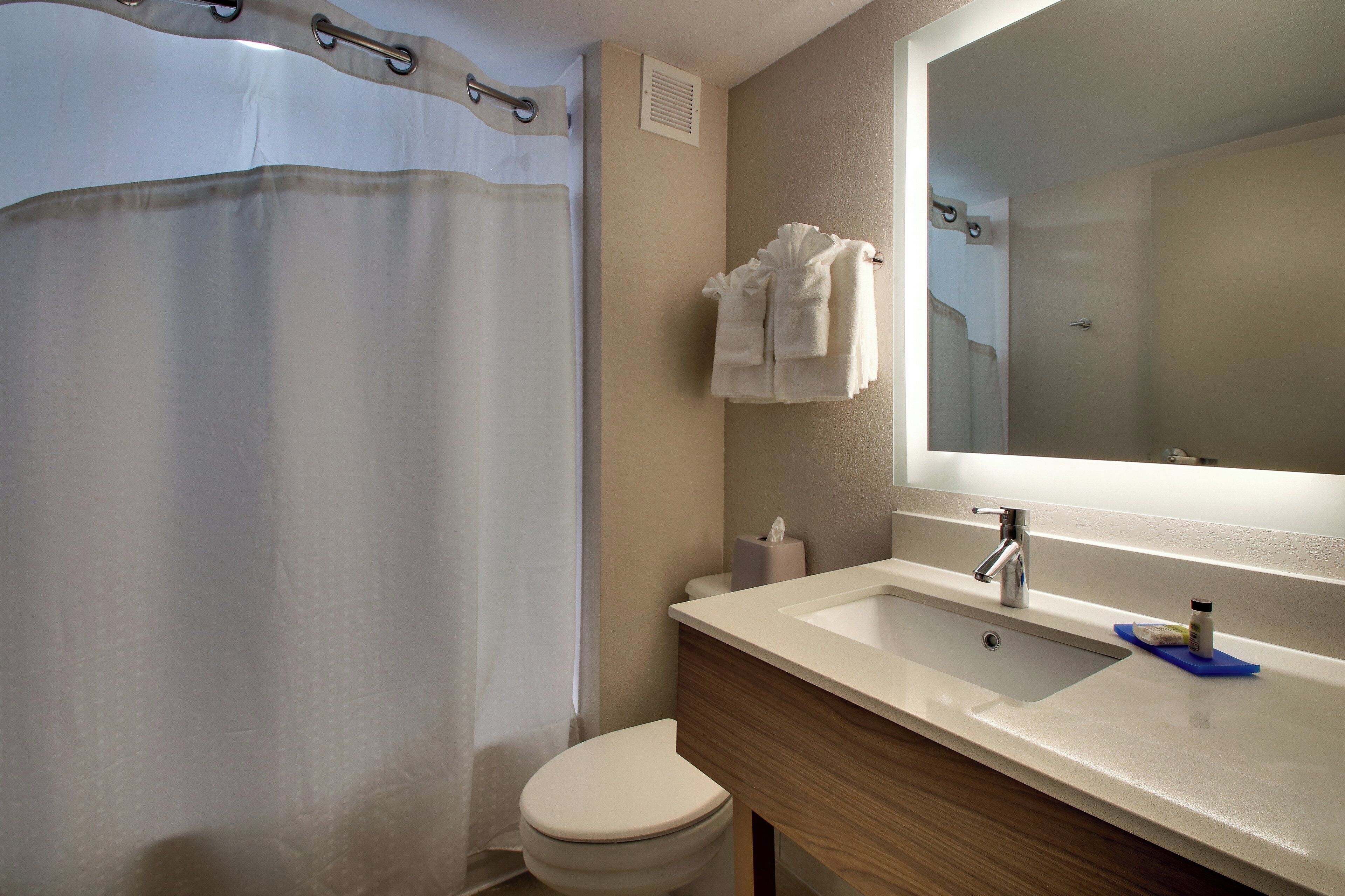 Un baño con cortina de ducha, inodoro, lavabo con espejo y un perchero para toallas.