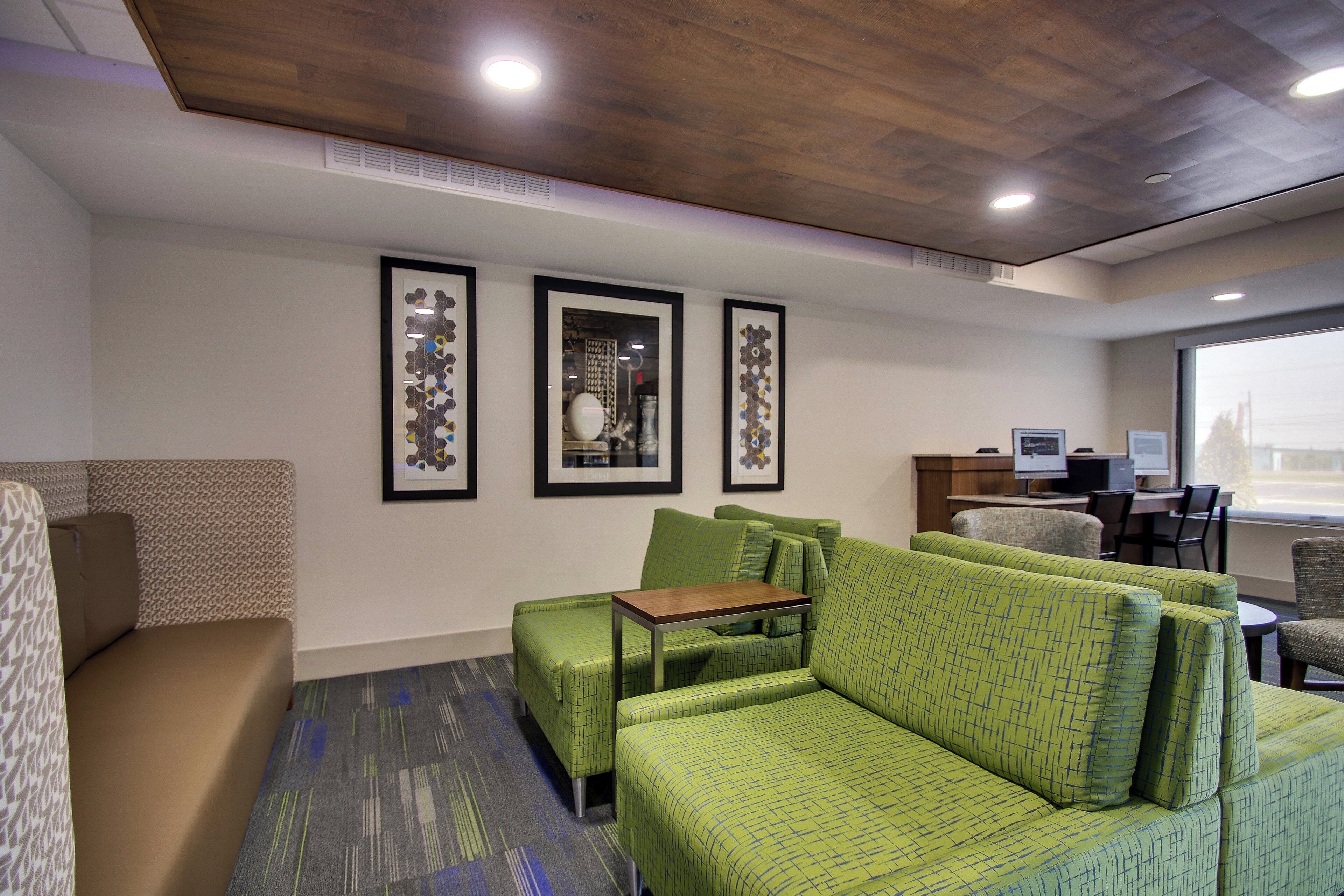 A hotel room with a green sofa set, a small table, and framed artwork on the wall.