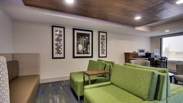A hotel room with a green sofa set, a small table, and framed artwork on the wall.