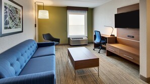 A hotel room with a blue sofa, a wooden desk, a flat-screen TV, and a large window with a view.