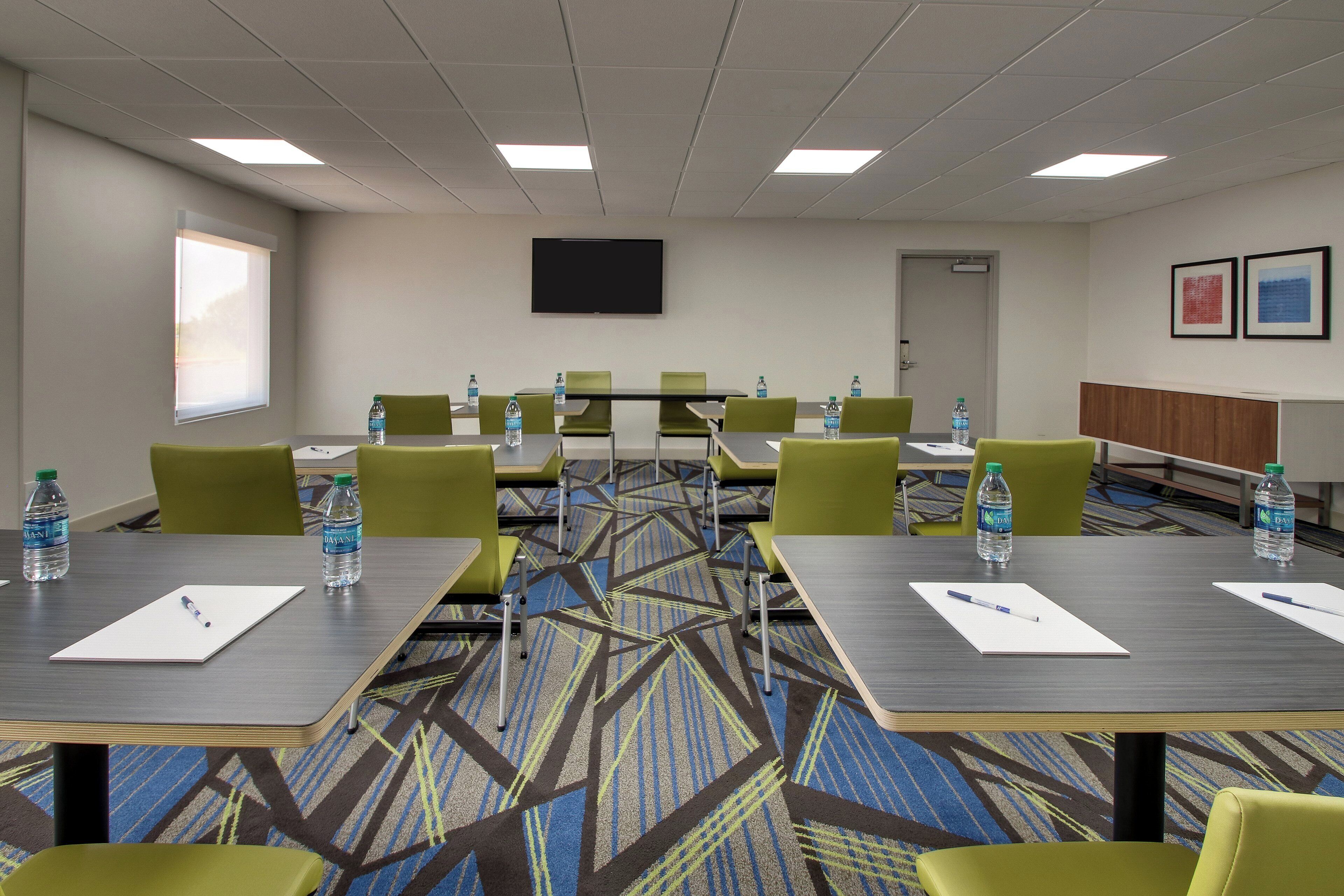 Une salle de conférence équipée de tables, de chaises, de bouteilles d’eau et d’un téléviseur à écran plat fixé au mur.