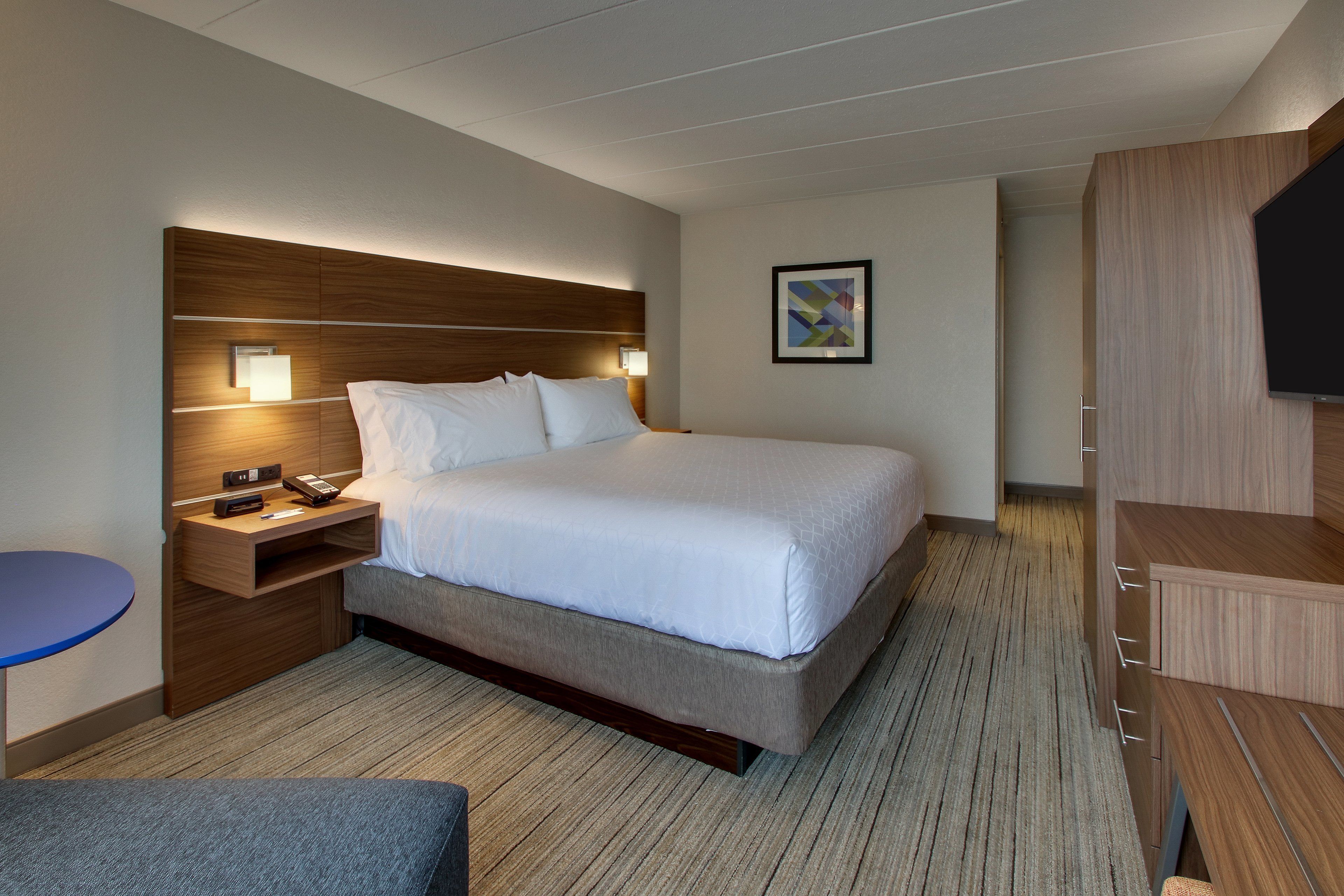 A hotel room with a large bed, bedside tables, a flat-screen TV, and a small seating area.