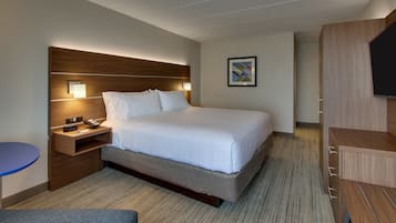 A hotel room with a large bed, bedside tables, a flat-screen TV, and a small seating area.